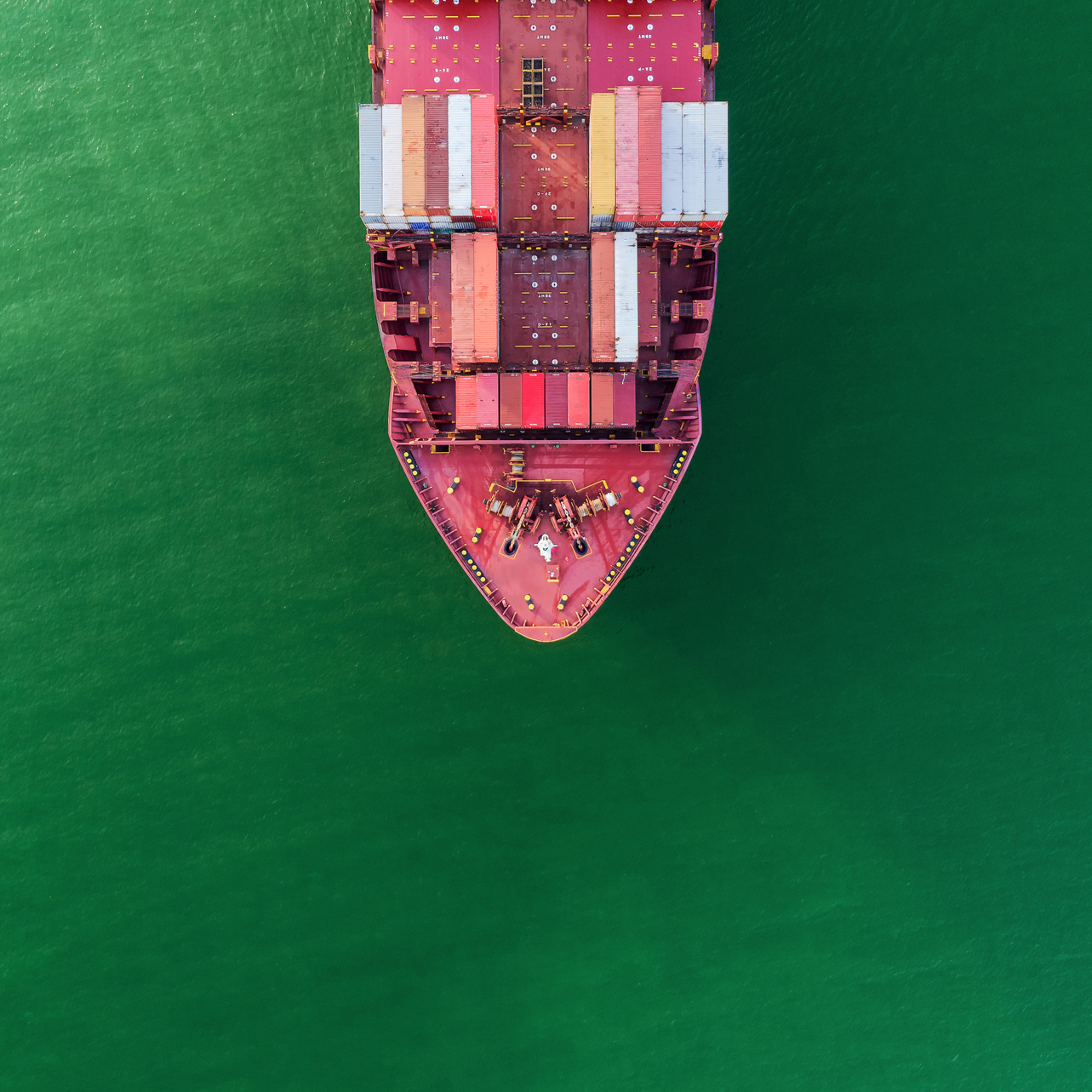 An aerial top-down view of a container ship on the sea going to quayside for load and unload