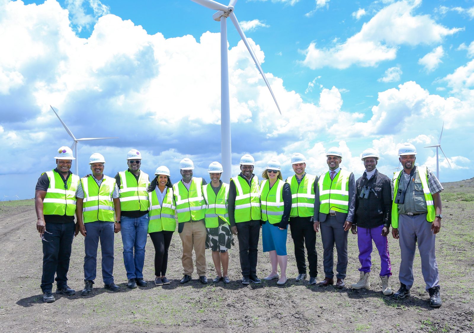 Director Ebong and USTDA Africa team members stand in front of wind turbines during tour of Kipeto Wind Farm.