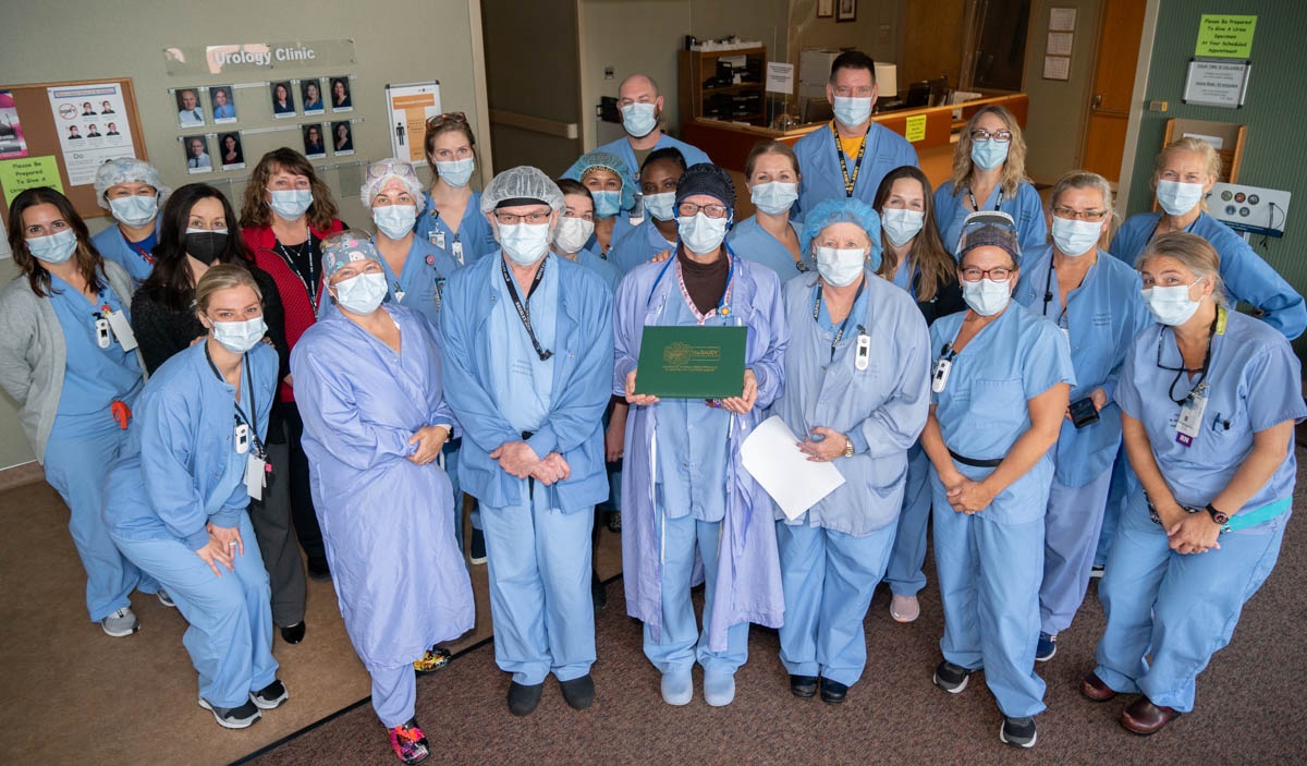 photo of a large group of people wearing blue scrubs and face masks in a hospital, one person is holding an award