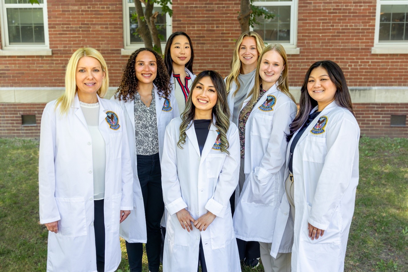 A group of women of various races and hair colors, all in white lab coats.
