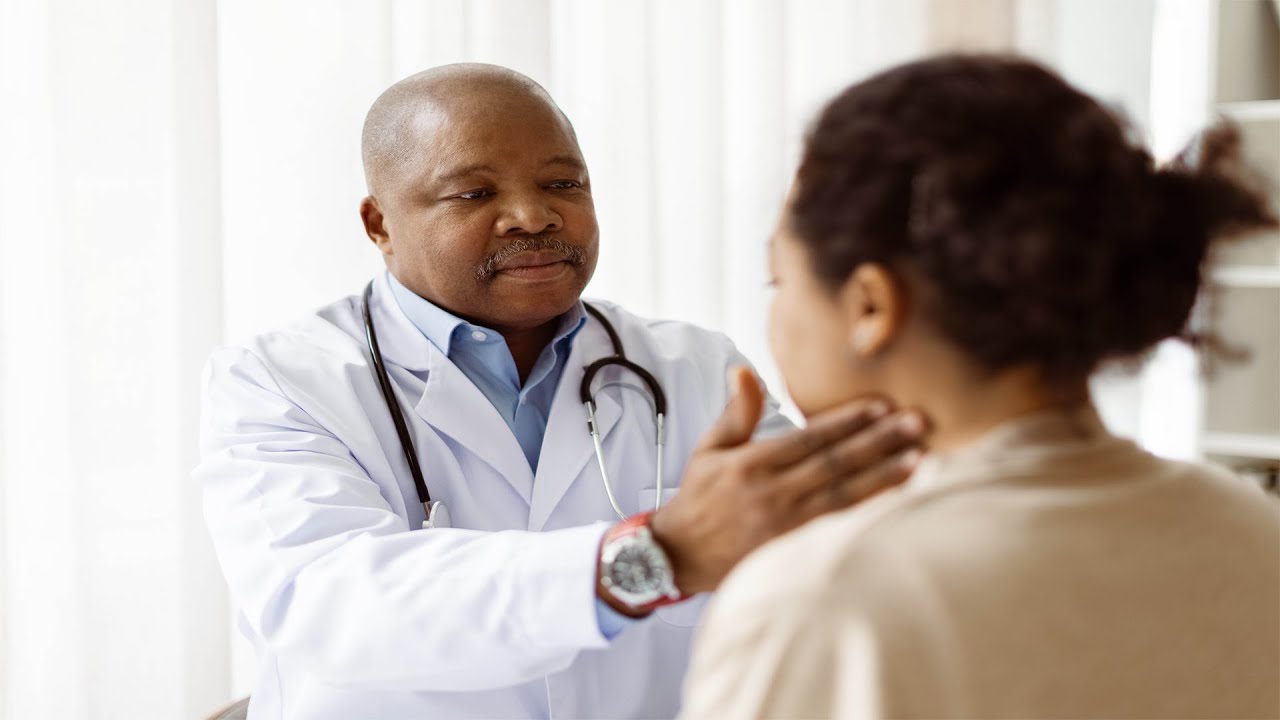 Male doctor in white coat examining a female patient's neck.