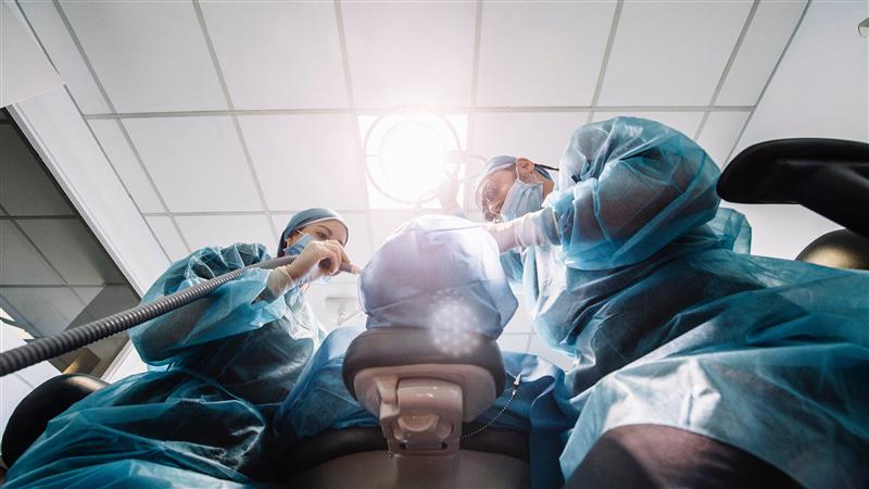 Two surgeons in blue gowns performing surgery on a patient.