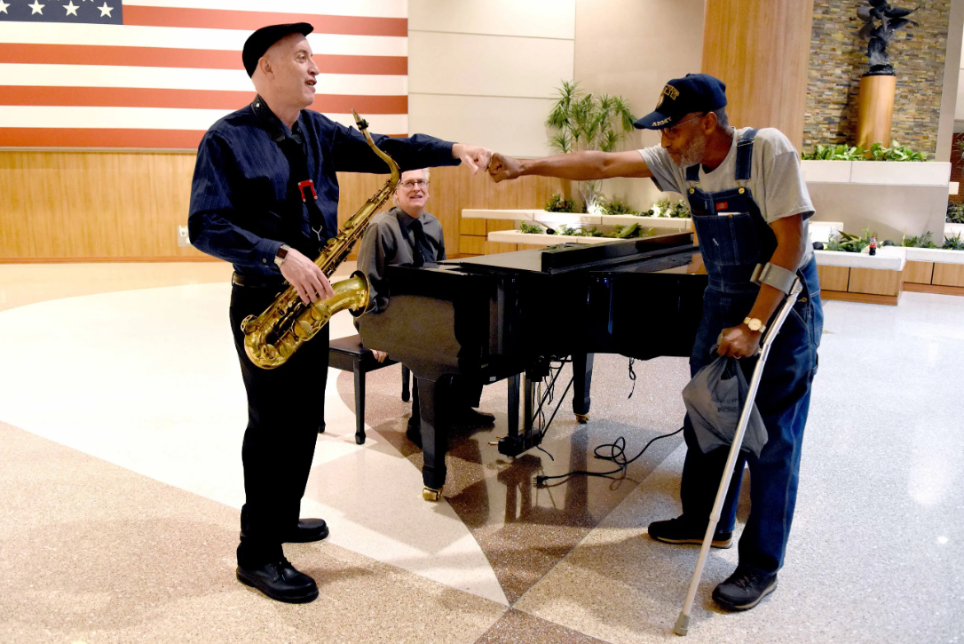 Veteran gives appreciation fist bump to saxophone player, while standing by a piano.