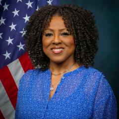 African-American woman pictured in front of an American flag wearing a blue shirt. 