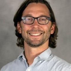 Headshot of a man with dark hair, eye glasses, button-up shirt.