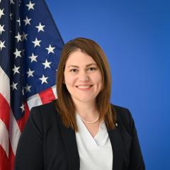A woman posed in front of a blue background and American Flag.
