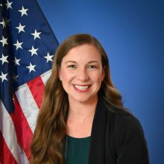 A woman posed in front of an American flag and blue background.