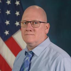 Shawn Rogan wearing glasses and a blue dress shirt with a tie.