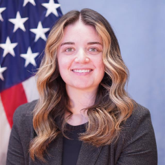 Woman with blonde hair smiling in front of an American flag.