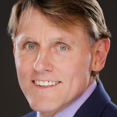 Portrait of a man in a blue suit and purple shirt smiling.