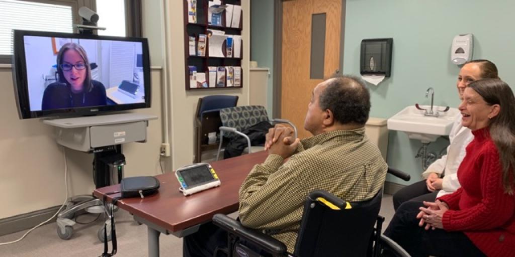 Three people sitting in front of a tv screen talking with someone on the screen.