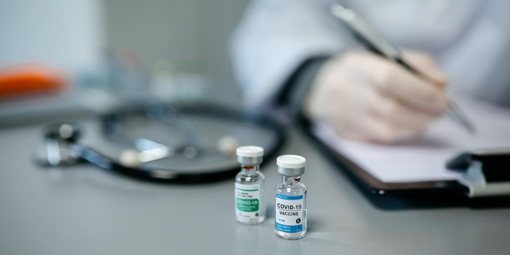 Doctor with pen next to vial of covid-19 vaccine