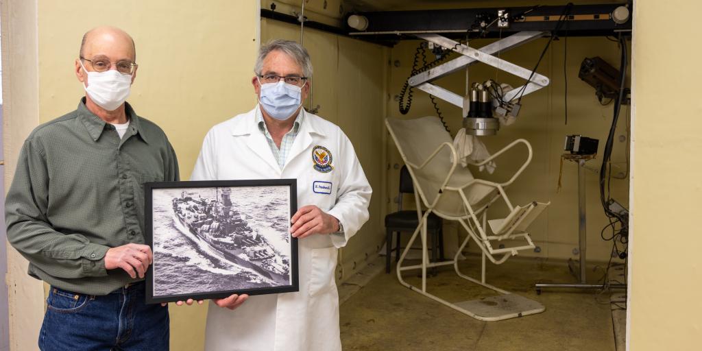 Dr. Nicholas Friedman and Paul Kanabrocki hold a picture of the USS Indiana in front of Edward Hines, Jr. VA Hospital's retired whole-body radiation counter. The  device was completed in 1966 using 65 tons of the USS Indiana and was retired in 1995.