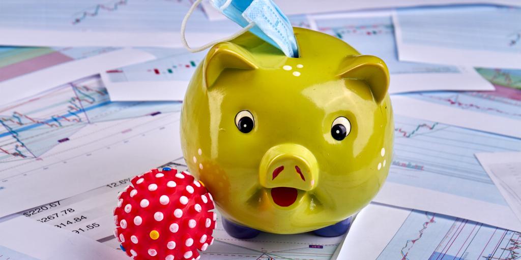 Piggy bank sitting on stack of photos with a surgical mask inserted.