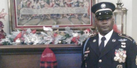 Army Veteran Terry Tisdale stands next to the fireplace in his in military uniform.