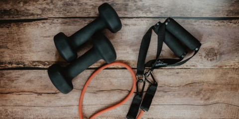 Set of dumbbell weights and jump rope lay on top of wood flooring 