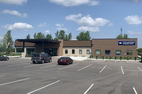 photo of a parking lot with a few cars and a brown, one-story building in the distance 