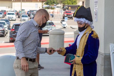 a man in colonial costume hands out information on voting