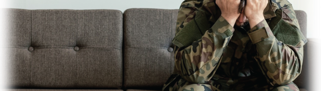 Photo of a soldier sitting on a sofa with his head in his hands in apparent mental distress.