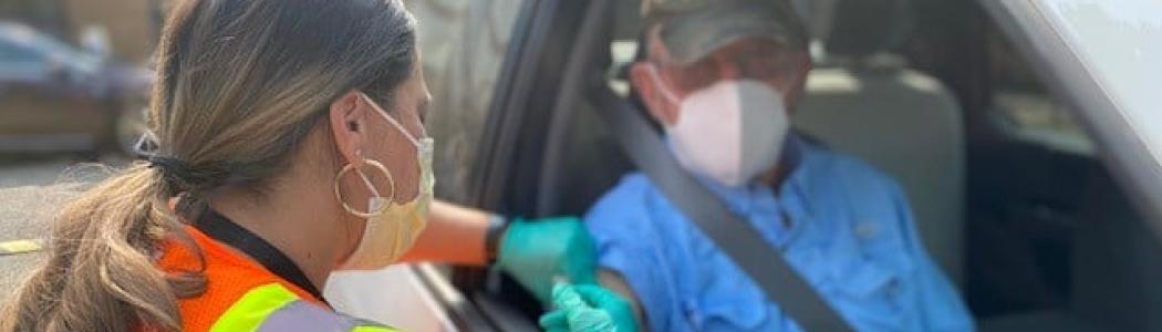 Nurse giving vaccination to man in car.